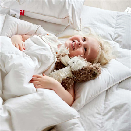 Glad pige ligger i en seng med Kiddy juniordyne og junior pude